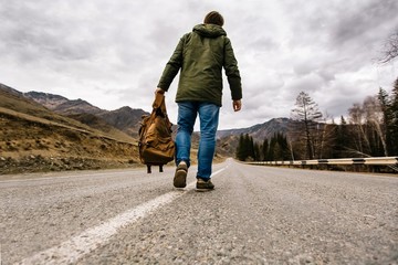 man with backpack in hand walking alone down a mountain road 