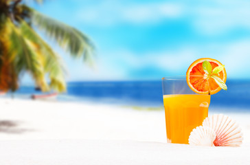 Orange juice and summer accessories on sand with tropical beach background