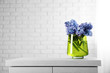 Beautiful hyacinth flowers in glass vase against brick wall background