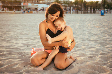 Portrait of a young single mother spending time with her son during holidays at the seaside. Woman touching her son with care, playing and hugging.