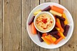 Plate of baby rainbow carrots with hummus dip, overhead view on a rustic wooden background