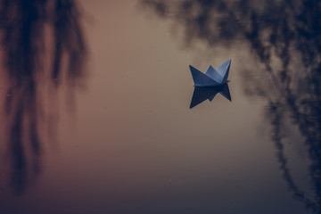 paper boat sailing on water surface at sunset