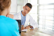 © AYAimages - Team of doctor and nurse discussing a patient diagnosis sitting at the desk in bright modern office