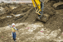 Worker Directing Digger At Construction Site