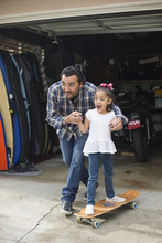 Hispanic Father Teaching Daughter To Ride Skateboard
