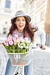 stylish woman in gray hat on a bicycle with spring flowers on a