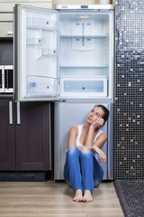 Unhappy and hungry girl near empty fridge