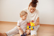 © WHstudio Leushin N - Happy family enjoying free time at home in sweet morning, sitting on the floor against white background, playing with toys. Caring young mother with her cute son spending weekend together