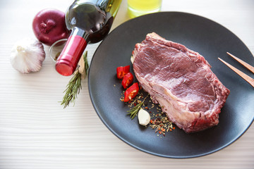 Canvas Print - Raw pork steak with bottle of red wine and spices on black plate