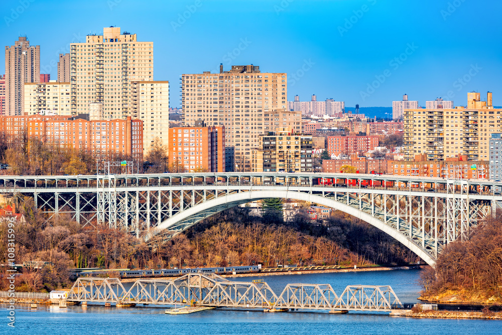Henry Hudson Bridge spans Spuyten Duyvel Creek, in New York City. Harlem apartment buildings shine under the late afternoon light. - obrazy, fototapety, plakaty 