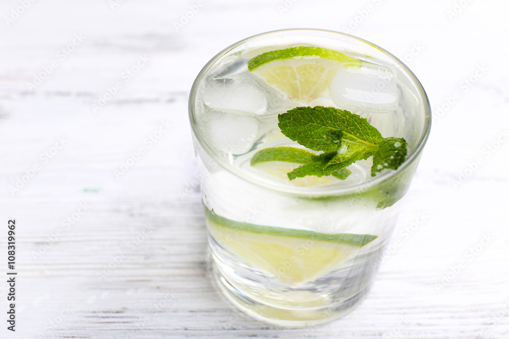 Fresh cocktail with ice, mint and lime on white wooden table background