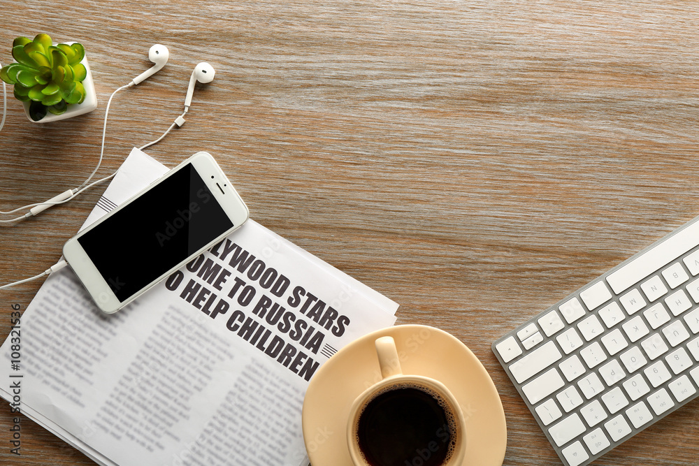 Workplace with mobile phone, keyboard and newspaper on wooden table