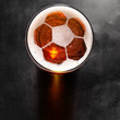 soccer or football ball symbol on foam of fresh lager beer glass on black table, view from above