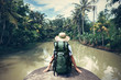 Woman traveler with backpack sitting on the edge and looking at tropical river (intentional vintage color)