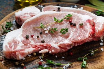 two pieces of raw pork on a wooden cutting board and spices