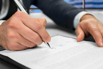 Mature businessman's hand signing document. Man signs paper beside window. New insurance policy. Official letter to a partner.