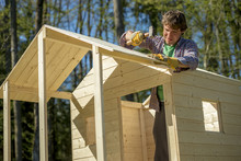 Young Man Using A Mallet To Fix A Nail Into A Roof Of A Wooden P