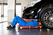 © twinsterphoto - Mechanic in blue uniform lying down and working under car at auto service garage