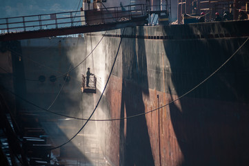 Shipyard worker power washing a ship on dry dock.