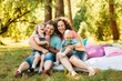 © SPY_studio - Young happy family with kids having picnic with colored pillows outdoors. Parents with two children relax in a sunny summer garden. Mother, father, little girl and baby boy playing in park.