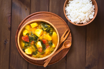 Canvas Print - Pumpkin, mangold, potato and tomato curry dish in wooden bowl with rice, photographed with natural light