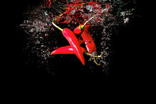 Several Red Peppers Fallen Into The Water Isolated On The Black Background