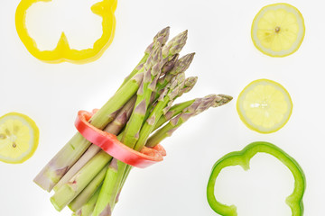 Wall Mural - Bunch of asparagus spears with lemon slices and bell pepper rings, on white background