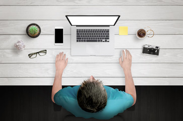 Fototapete - Man work on laptop with white isolated screen. Work desk with plant, camera, coffee, smart phone. Top view.