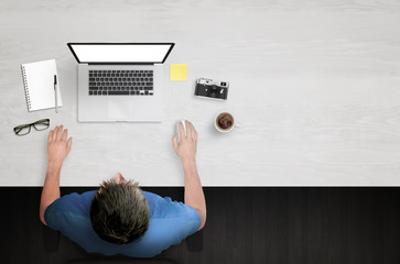 Poster - Man work on laptop with white isolated screen. Work desk with paper, camera, coffee, notepad, glasses. Top view.