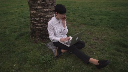Poster - Young businesswoman talking on the mobile phone and typing  on the laptop. Attractive mixed race caucasian model using app on smartphone.  Beautiful professional woman work outdoor. She wearing slip