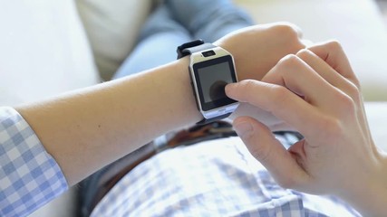 Man lying on sofa at home using smart watch