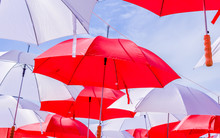 Hanging Multicoloured Umbrellas Over Blue Sky. Red And Withe Large Size Umbrellas Onto The Blue Sky. 