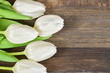 White tulips on left side of wooden background. Space for text.