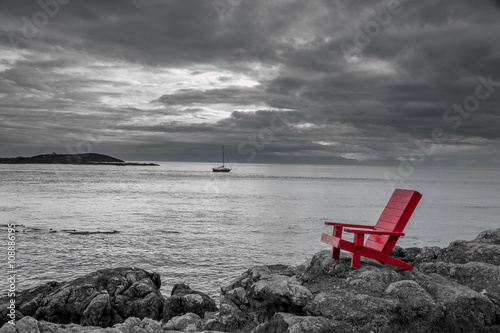 Naklejka dekoracyjna Red chair contrasting with black and white ocean background.