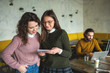 © katie_martynova - Two young females with smartphone and tablet in cafe