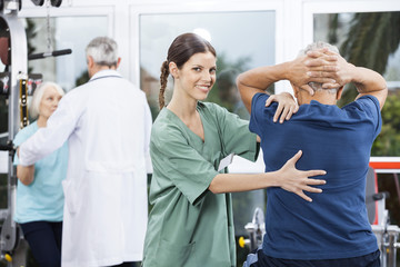 Wall Mural - Female Nurse Assisting Senior Man In Back Exercise