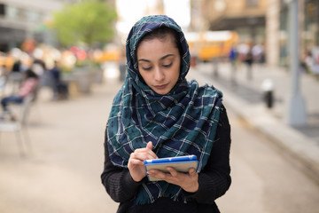 Young woman wearing hijab in city using tablet computer