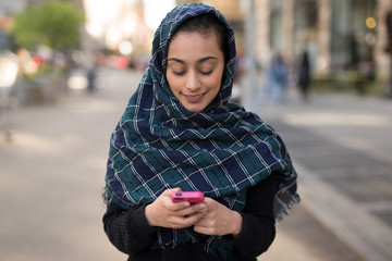 Wall Mural - Young woman wearing hijab in city texting on cell phone