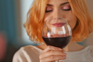 Young woman with glass of red wine on blurred background