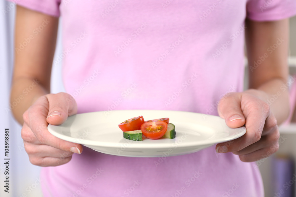 Female hands holding a plate with tomato and cucumber slices.