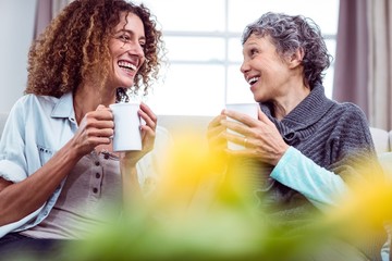 smiling mother and daughter holding coffee mugs while discussing