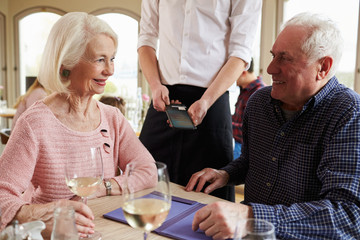 Wall Mural - Senior Couple With Waiter Paying Bill In Restaurant