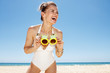 © Alliance - Smiling woman at sandy beach holding funky pineapple glasses