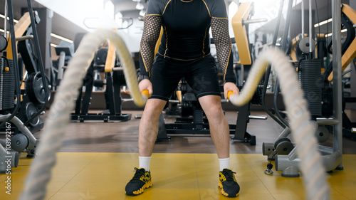 Photographie Man training with battle rope in fitness club