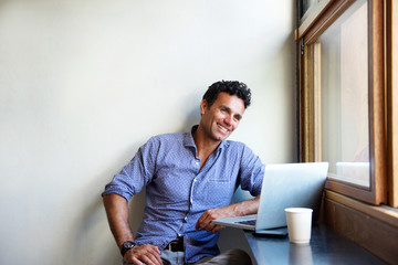 Mandsome modern man smiling with laptop at cafe