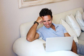 Wall Mural - Smiling man sitting at home with laptop