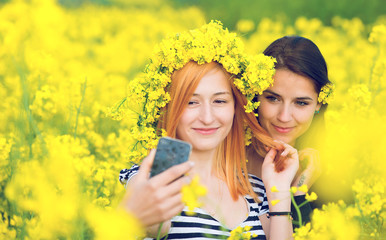 Two friends taking a selfie in a field with  yellow flowers of rapeseed