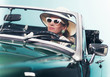 Woman in retro 1960s fashion with hat and shades driving convert
