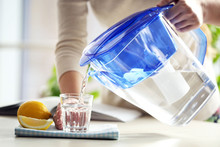 Woman Pouring Water From Filter Jug Into Glass In The Kitchen
