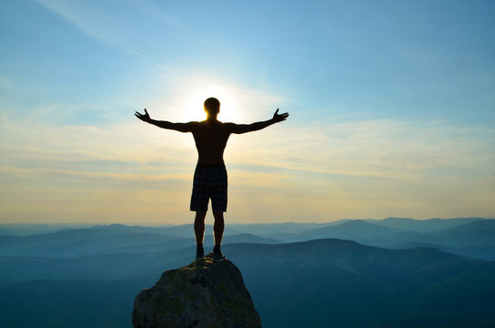 man stands on top of a mountain with open hands